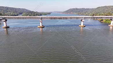 Aerial side-view of a truck crossing a large bridge spanning a wide river in a scenic, tropical valley in rural India