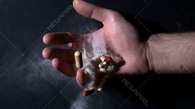 Hand holding white powder and pills dropping dead