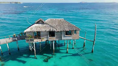 Tropical bungalow with thatched roof stands on stilts in turquoise ocean water paradise view