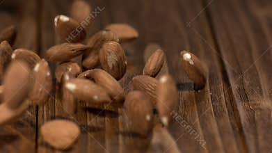 Almonds drop on wooden surface in slow motion during a cooking session in a kitchen