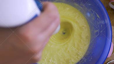 Female hand controls hand mixer above blue bowl