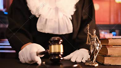 Judge in robe and gloves striking gavel in courtroom