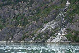 Floating chunks of in front of falling water and geologic structures at Endicott Arm near Dawes Glacier