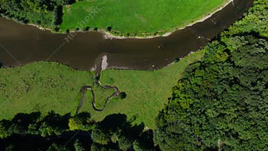 Top view of winding river crossing grassy land surrounded by forest edges