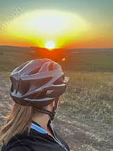 Cyclist wearing helmet watching golden sunset over rural landscape