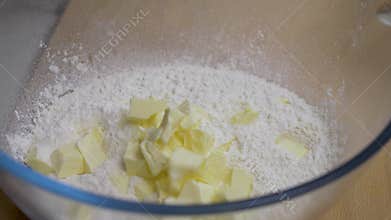 Cubes of butter fall onto pile of flour in glass bowl