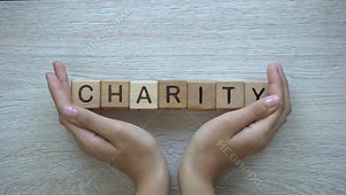 Charity, hands pushing word on wooden cubes, donations and helping in need