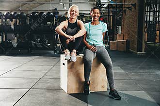 Smiling women sitting on a box together after working out