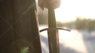 Man in medieval suit holding sword. Action. Close-up of man`s hand in medieval suit holding sword hilt on background of