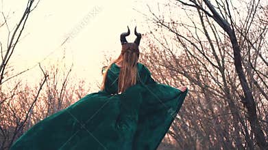 Horned stranger in long emerald silk dress deep in forest alone with magic stick in hand, terrible vampire hiding from