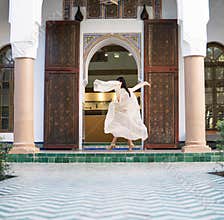 Beautiful Moroccan Girl Waving her white mantle in Rich interior of Picturesque Dar Si Said Riyad in Marrakech