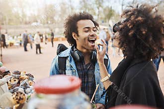 Side-view of cute african-american couple in love having fun in park during food festival, standing near counter and