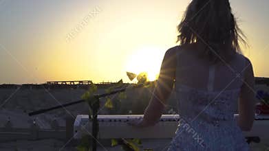 Young blonde woman with plays romantic music on digital piano at sunset. Pretty girl sings performs on stage with sun on