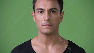 Young handsome Hispanic man against green background