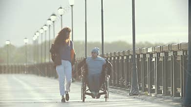 Disabled man in a wheelchair walking together her girlfriend on the quay
