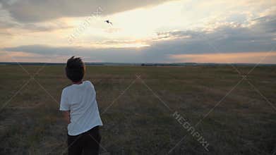 A boy in the field at sunset runs and throws a paper plane. The concept of a happy child