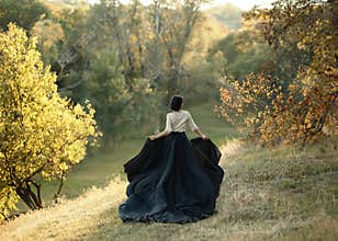 Princess in a vintage dress. Walk along the picturesque autumn hills at sunset. A long train of black skirt fluttered on the run.