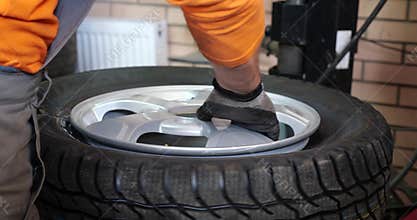 Sservice man put on tyre on car wheel by special tool, mechanic using mounting tool for tire repair