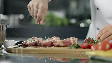 Male chef salting meat at kitchen. Closeup chef hands salting steak at workplace
