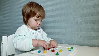 Baby girl sits at a childs table and collects a mosaic close up in slow motion
