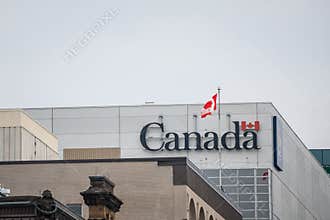 Canada Wordmark, the official logo of the Canadian government, on an administrative building next to a Canadian flag waiving