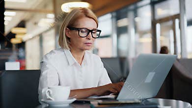 Busy entrepreneur senior woman working with laptop typing in modern cafe