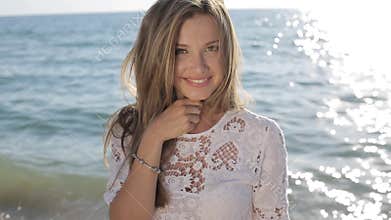 Beautiful sexy woman with blond hair in elegant dress posing on the beach, smiling on camera