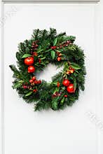Green christmas wreath with pomegranate and red berries on white door.