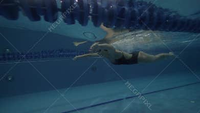 Woman swimmer in black swimsuit floating breaststroke under water in pool