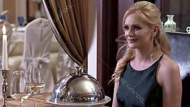 Waiter opens tableware cover - cloche showing the dish in front of the blonde girl. Fine dining restaurant concept.