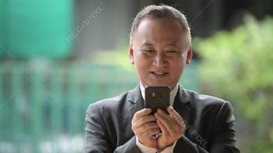 Mature Japanese businessman using phone in the streets outdoors