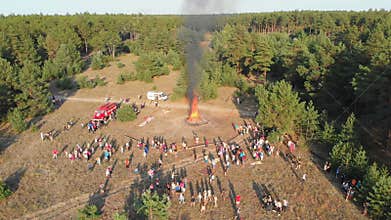 Aerial view of the organized gathering of people near a large campfire in a pine forest