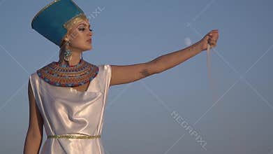 Egyptian wife of Pharaoh lets out a handful of sand posing in the desert at sunset