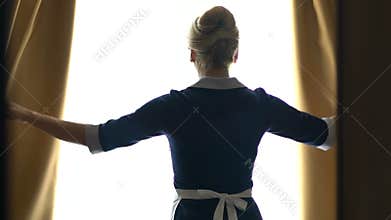 Chambermaid of luxury hotel opening curtains in best suit, going to clean room