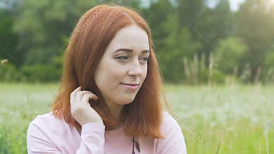 Shy beautiful woman looks down up outdoors in summer field, red haired female