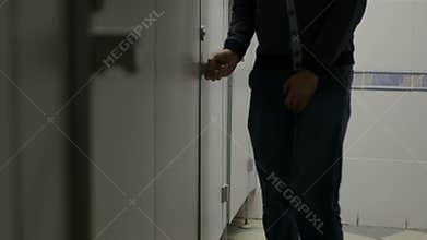 Man with urinary incontinence in public restroom near closed toilet cabin
