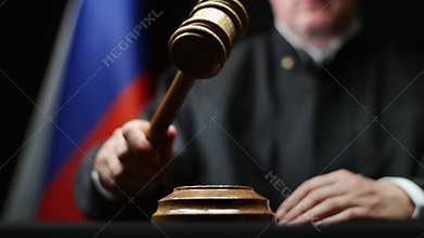 Judge with gavel in his hand hammering against Russian flag and black background in court room