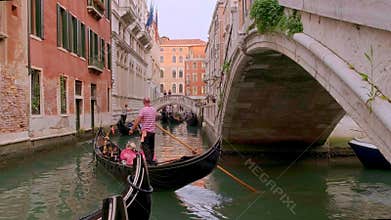 Gondola go down canal at day, Venice, Italy. Gondolier navigate boat. Tourists enjoy ride and take photos. Medieval