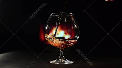 Woman pours cognac into a glass on the background of the fireplace.