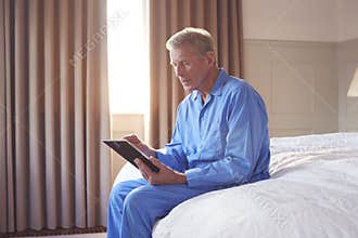 Bereaved Senior Man Sitting On Edge Of Bed Looking At Photo In Frame