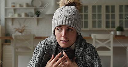 Frozen woman sits at home wrapped in plaid wearing hat