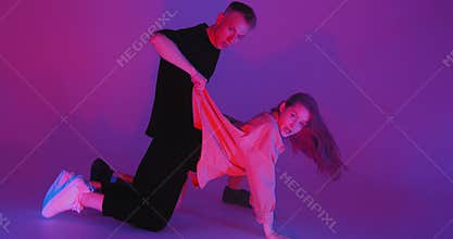 Dancing young couple in colourful neon studio light quickly moving with passion. Contemporary dance, hip hop dancers