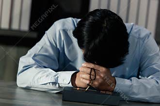 Asian man bowing his head on the Bible and carrying a cross. According to the beliefs of Christianity Is the salvation of Jesus.