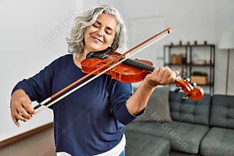 Middle age grey-haired artist woman playing violin standing at home