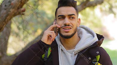 Handsome bearded hispanic man talking on mobile phone at forest trees background, millennial arabic guy answering call