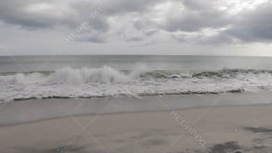 Wave breaking on the beach in slow motion, ocean and cloudy gray sky. Calm, serene, sad atmosphere.