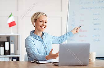 Online foreign languages tutoring. Joyful teacher giving Italian class, pointing at blackboard with basic grammar rules