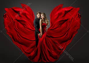 Fashion Couple in Love. Woman in fantasy long Red Gown and handsome Man. Flying Silk Fabric as Wings. Studio Portrait