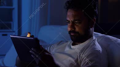 indian man with tablet pc in bed at home at night