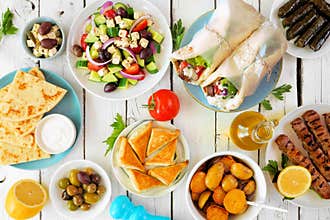 Greek food table scene, above view on a white wood background